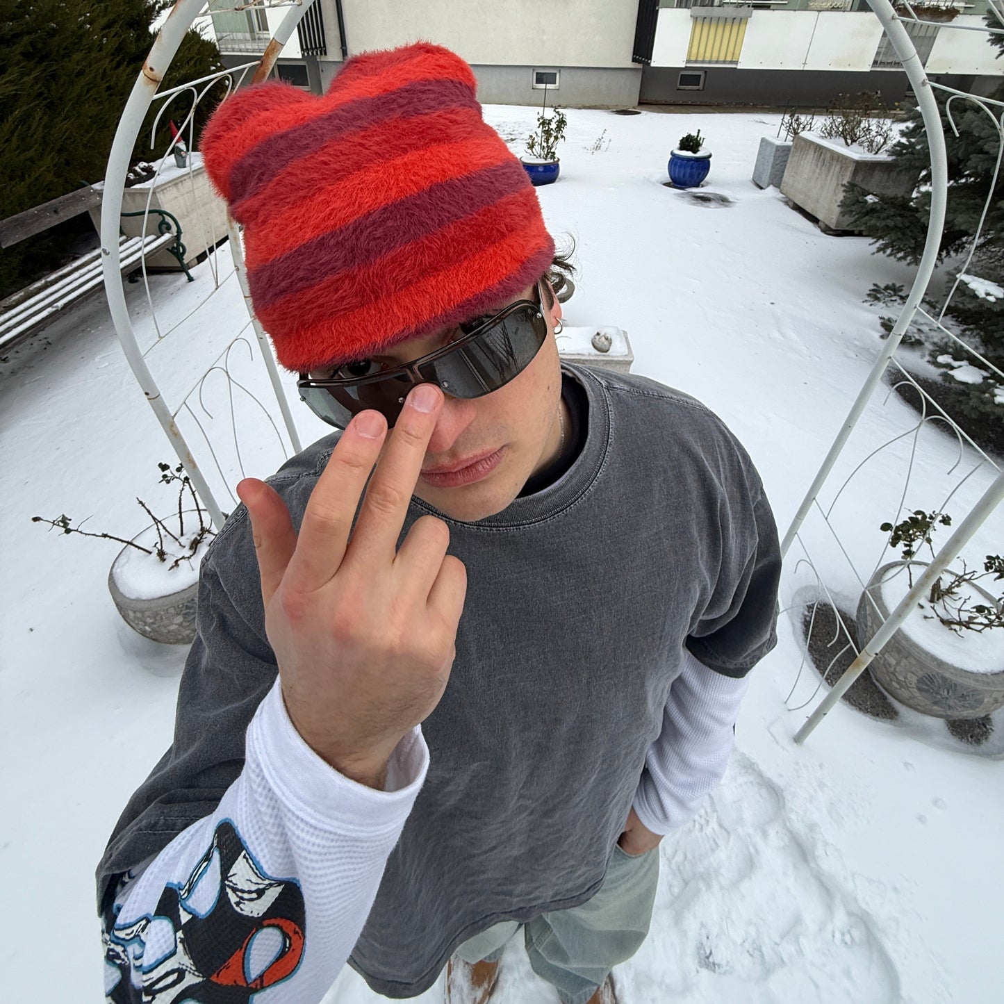 Person wearing a red and burgundy striped fuzzy beanie and sunglasses in the snow.